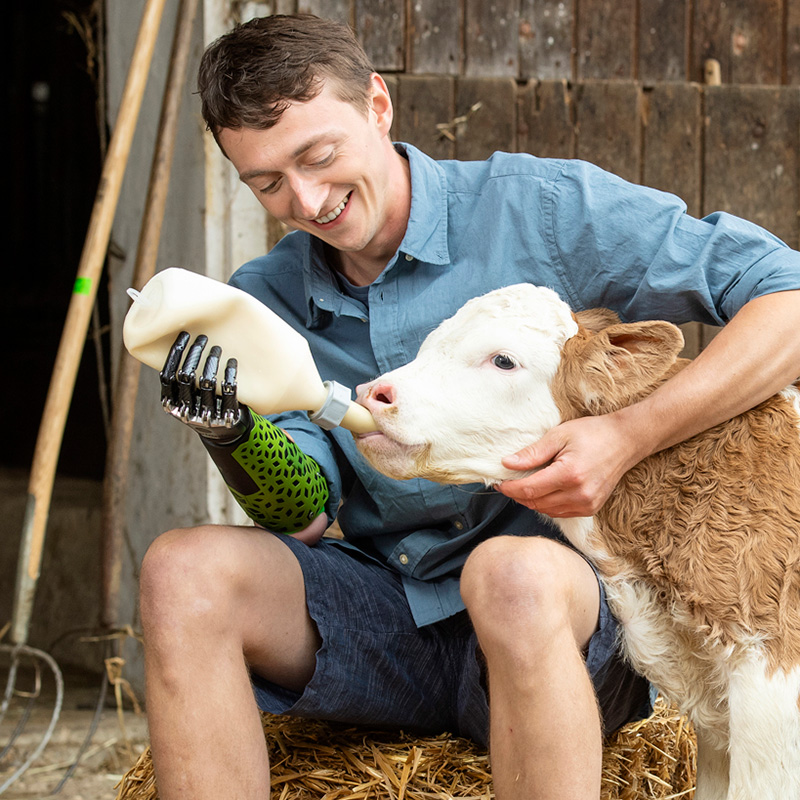 Foto Mann mit einer Armprothese der ein Kalb füttert